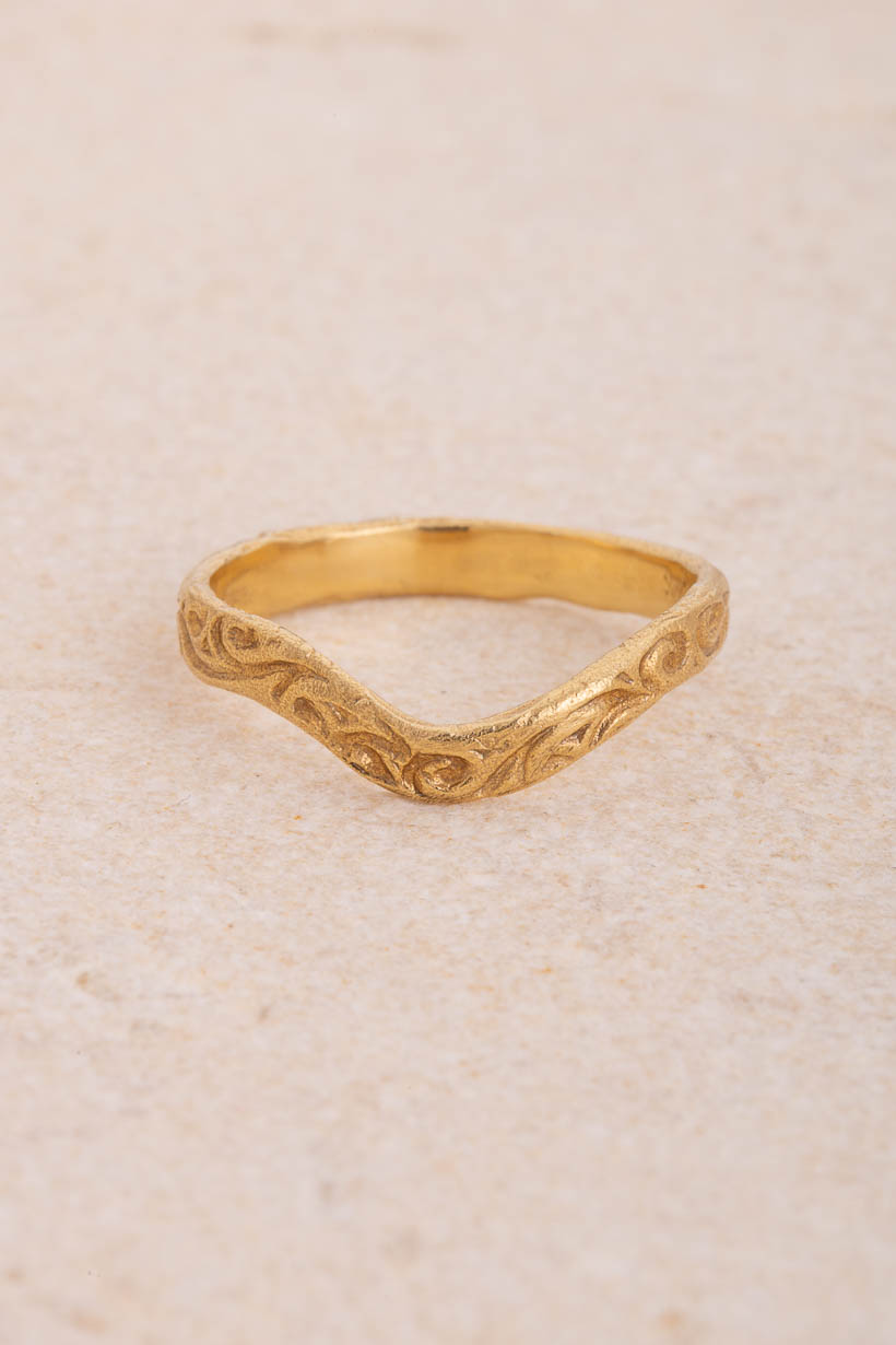 Whisper curved 3mm wedding band with faint hand-engraved swirls in recycled gold, shaped to sit snugly beside an engagement ring, handmade in Melbourne, front view on limestone