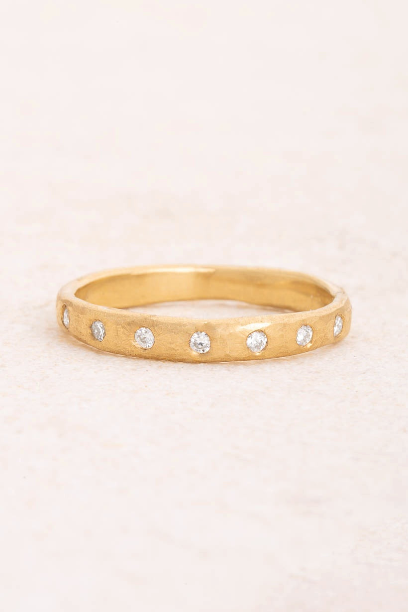 Dewfall diamond eternity band by Ada Hodgson, sixteen white diamonds flush set around a 3mm textured recycled gold wedding ring, flat lay