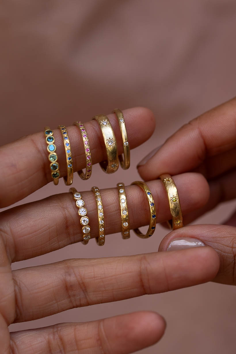 Handmade gemstone wedding bands and engagement rings stacked across several fingers, Australian sapphires and recycled gold rings by Ada Hodgson, Melbourne