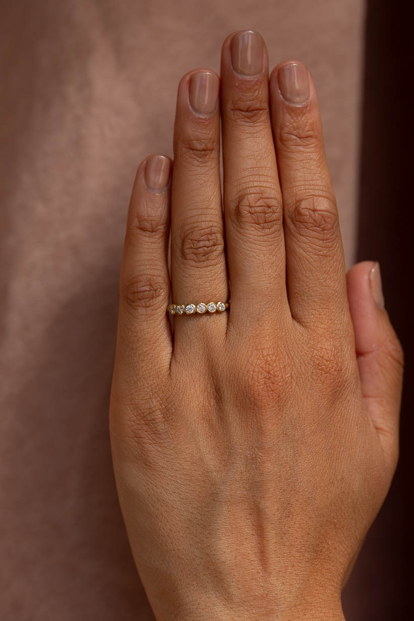 Gumnut diamond wedding band worn on the hand, six bezel set white diamonds on a textured gold band, Ada Hodgson