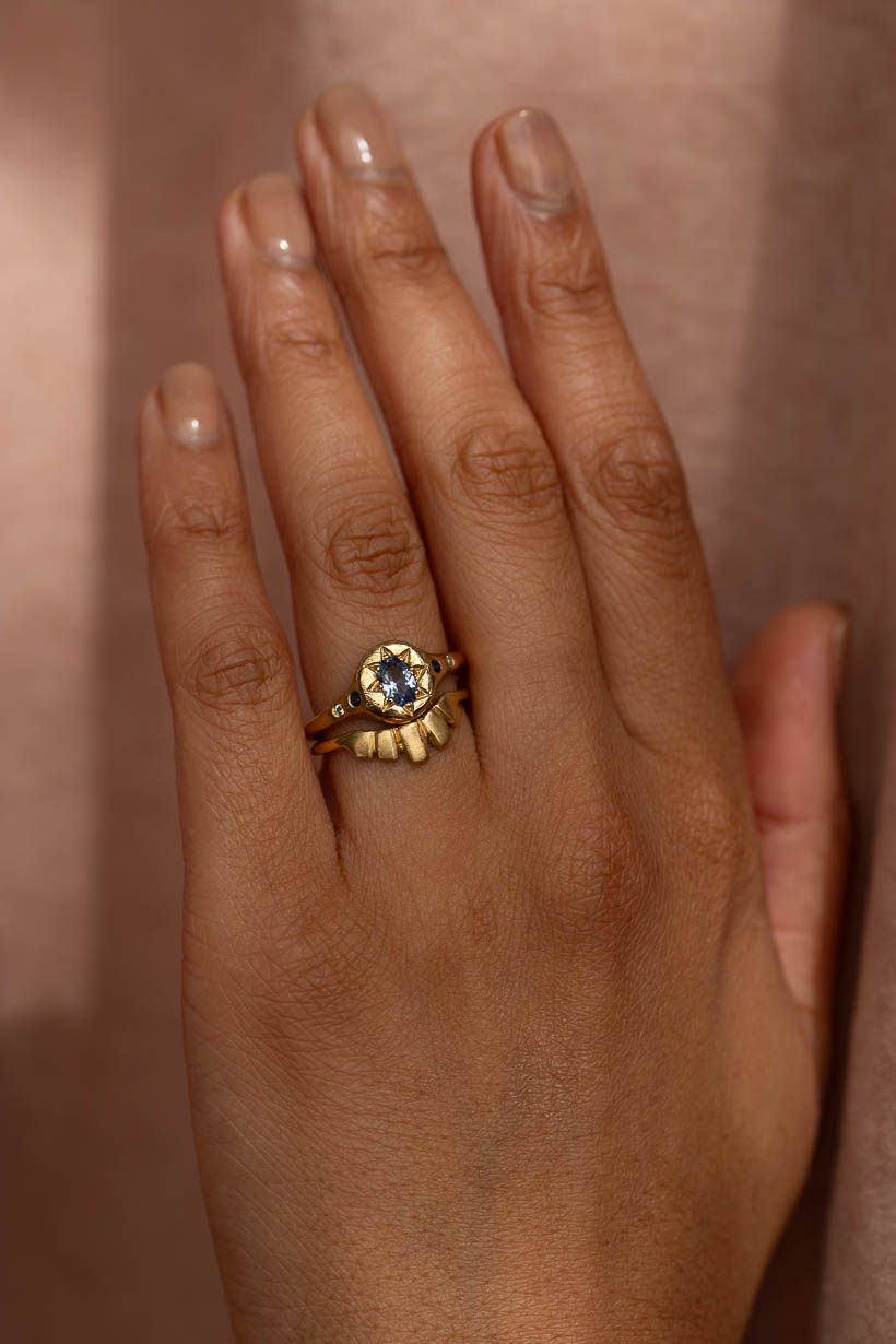Close-up of the Monet's Garden Ceylon sapphire engagement ring stacked with the curved Keystone wedding band in recycled yellow gold