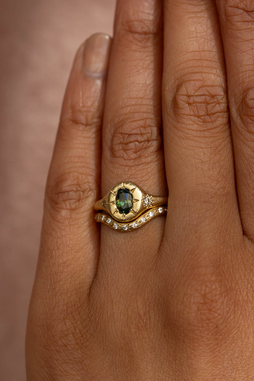 Side view on hand showing the tapered 2mm textured band and flower-set diamond. Monet's Garden signet style engagement ring with green Australian sapphire and two champagne diamonds flower set either side. Stacked with white diamond curved rosette wedding band.