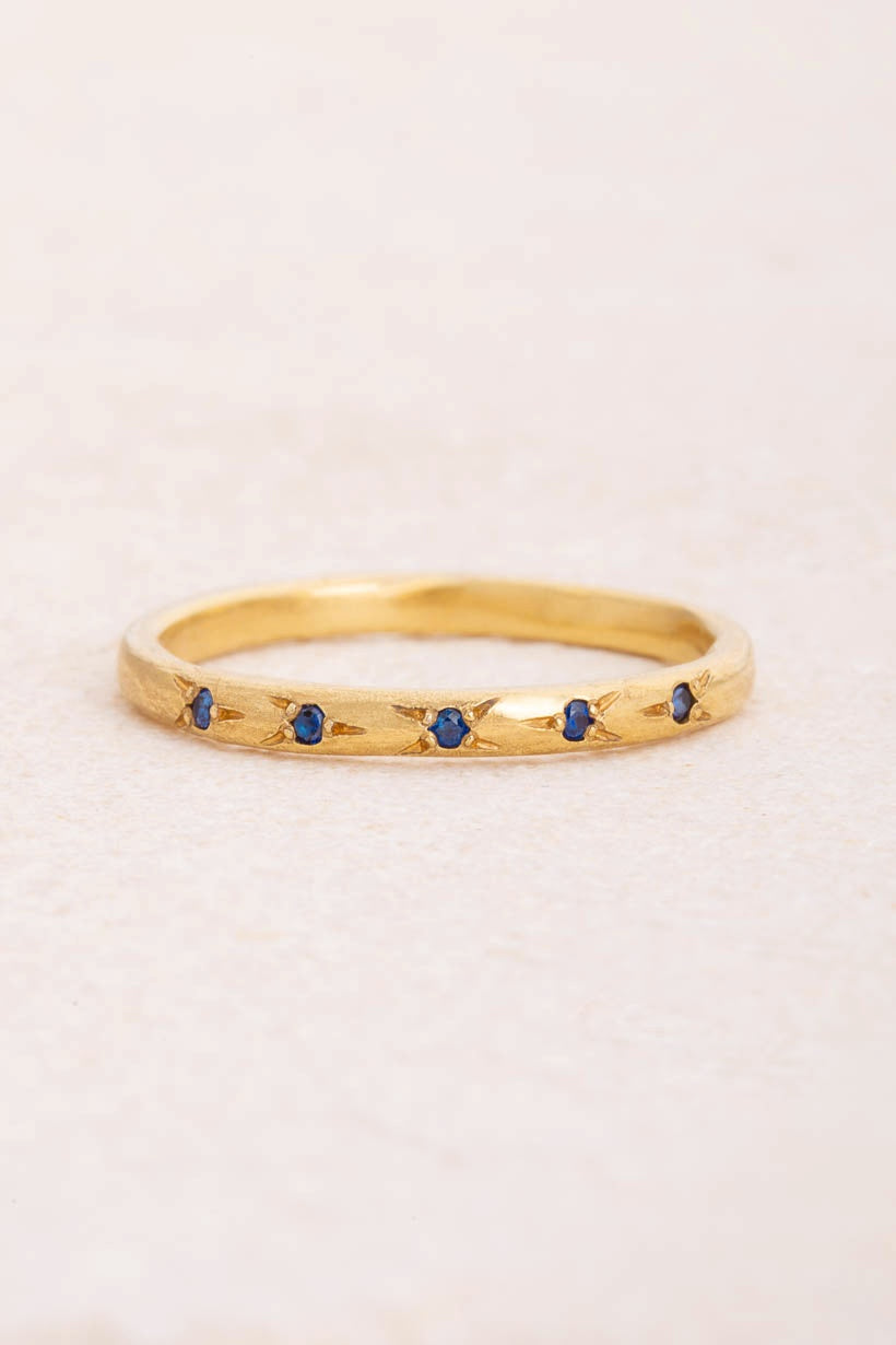 Flat lay of the Rosette ring with five flower-set deep blue Australian sapphires in textured recycled yellow gold