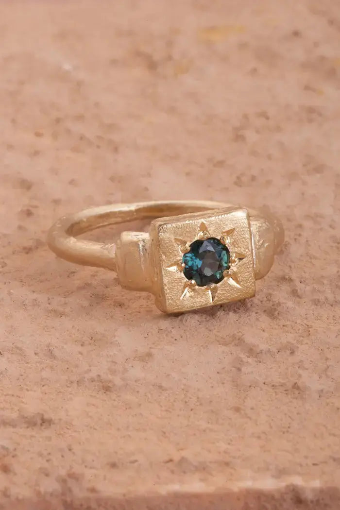 Flatlay of the Dawn Signet Ring in yellow gold with a teal topaz. A gold signet ring with lots of texture and a unique organic finish. 