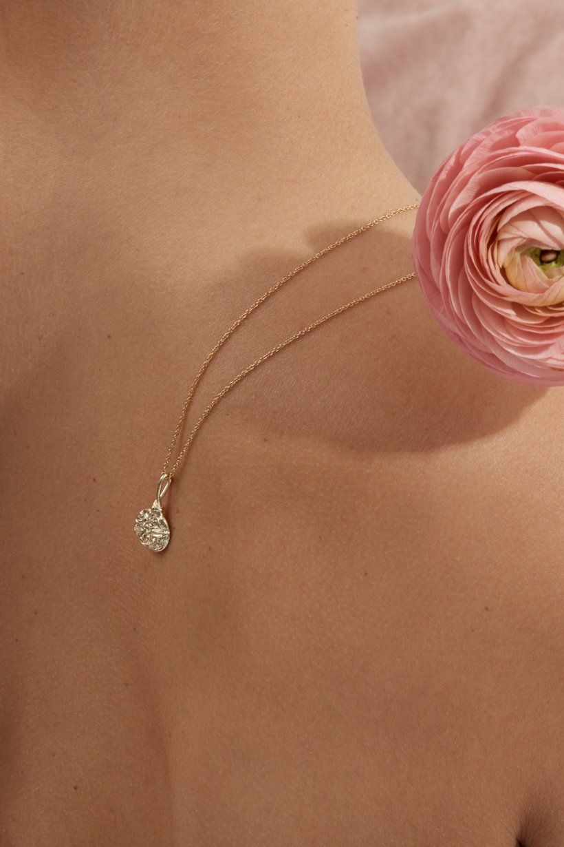 9ct yellow gold Floral Relic pedant on a fine gold chain laying over models shoulder with a flower