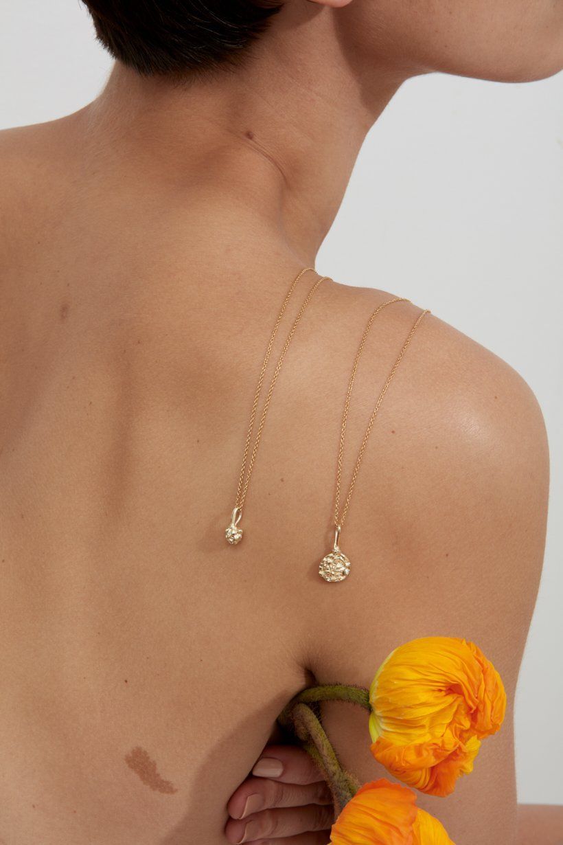 Floral Relic necklace and artichoke necklace in 9ct yellow gold hanging on models back with flowers 