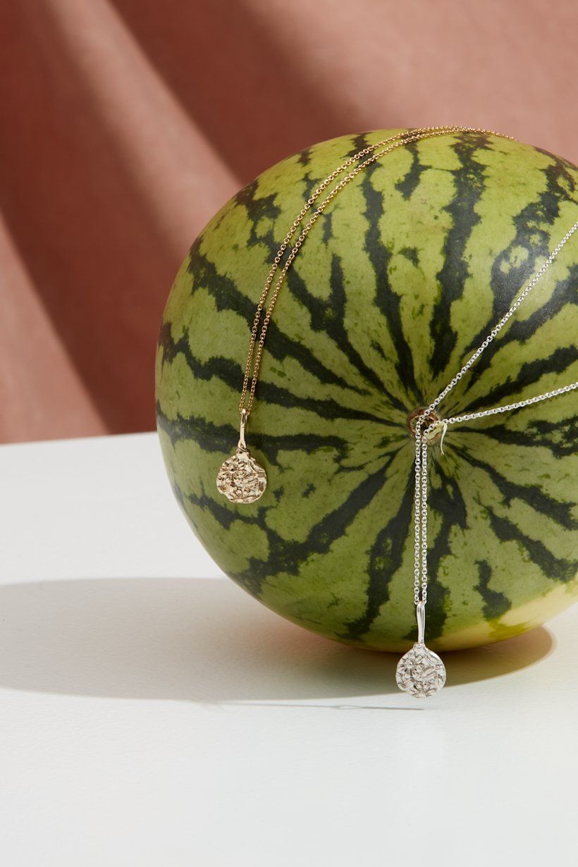 The gold and sterling silver floral relic pedants on fine chains laying on a watermelon. 
