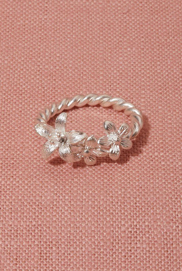 A sterling silver ring with a vine and floral design, displayed on a pink background.