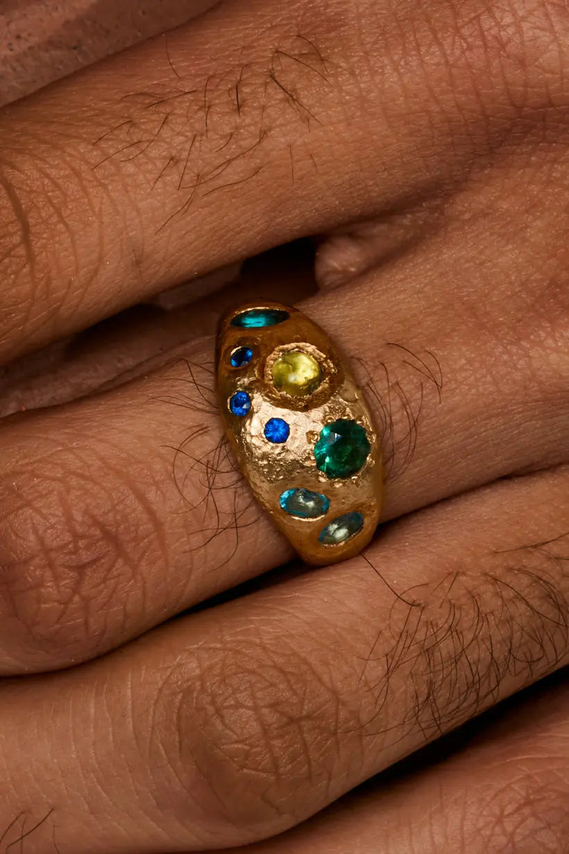 Close up of the Rockpool ring on a models hand. Bright blue sapphires sparkling in this textured wide gold band. 