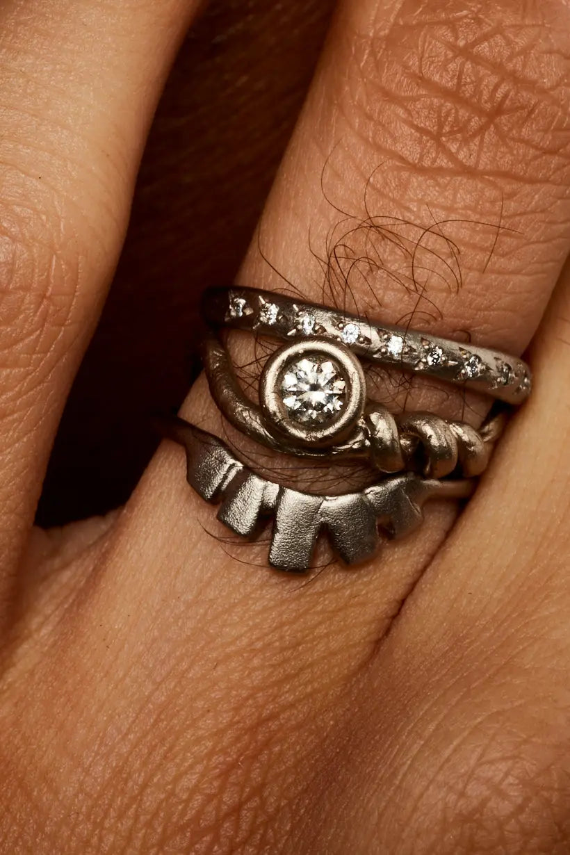 The Rosette Ring in white gold worn on a model’s hand, paired with a the white gold trailing ring and white gold curved wedding band, the Fountain Ring.