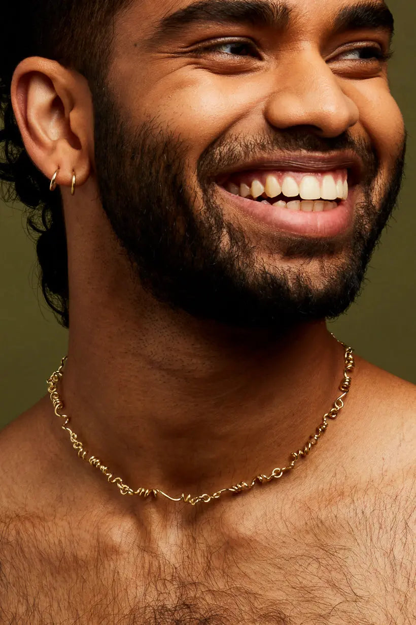 A smiling person wearing a 9kt yellow gold tendril necklace with a chain of gold.