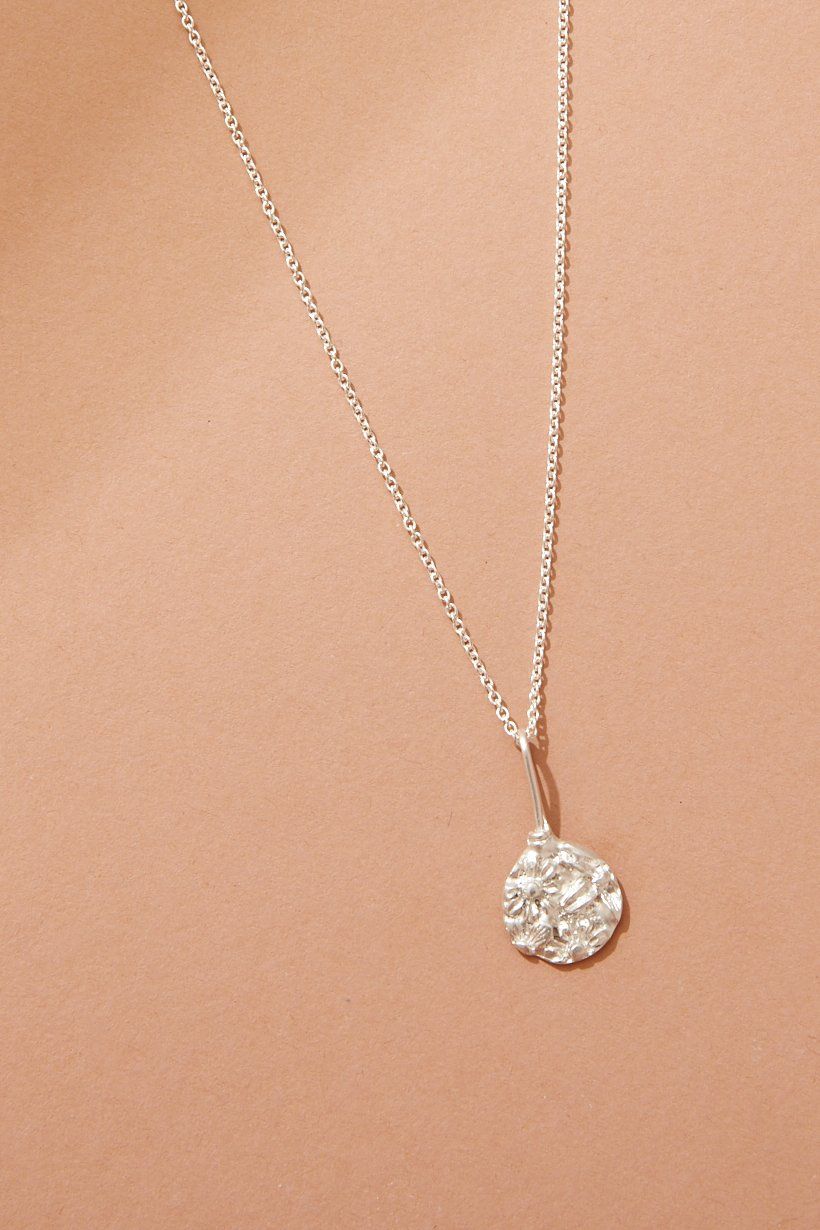 Floral Relic necklace laid flat on orange cardboard, with flowers pressed into metal in a round pendant