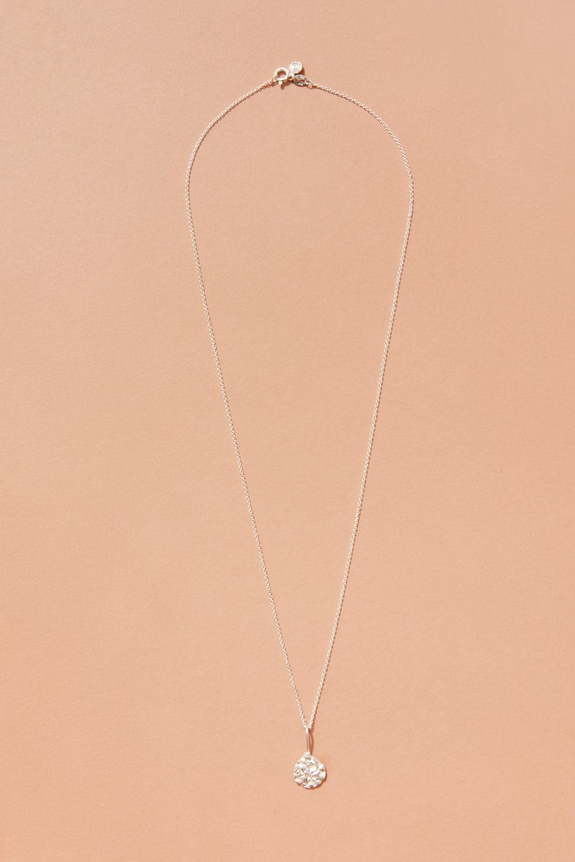 The whole Floral Relic necklace laid flat on orange paper, showing the length of the chain